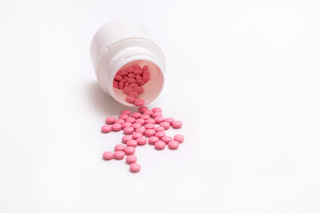 Pink pills spill out from bottle isolated on white background.