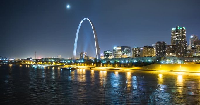 St. Louis, Missouri, USA - view of the illuminated city at night with the Gateway Arch monument and the Mississippi River with passing ship - Timelapse with pan left to right 