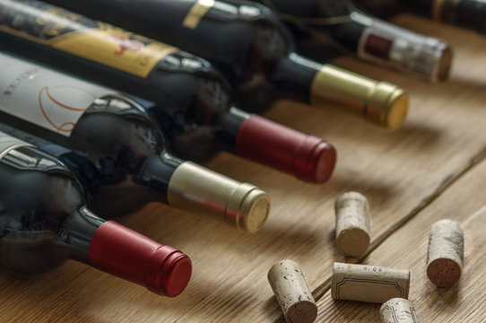 Row of red dry wine bottles and wine corks  on wooden background. Low depth of field. 