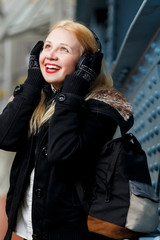 Fototapeta premium Cheerful ginger girl with headphones listening music at blue wall