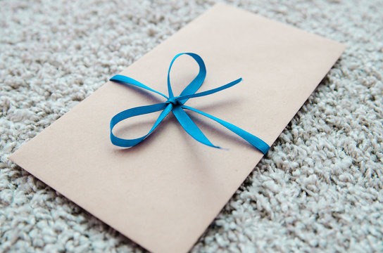 Gift kraft envelope tied with a turquoise ribbon tied on the bow on a gray background. The envelope for the card
