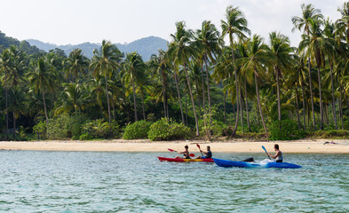 Koh Chang, Thailand MARCH 28, 2015; Tourists kayaking on sunny tropical beach with palm trees