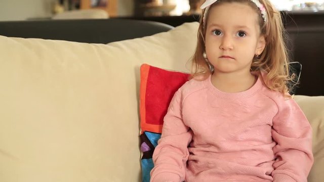 Beautiful little girl relaxing on a sofa in the living room and holding a TV remote