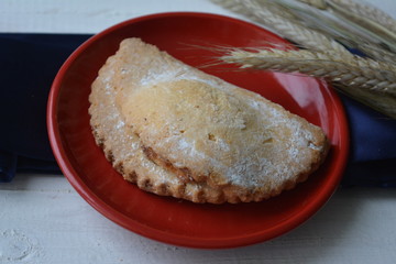ruddy delicious cookies with powdered sugar on a red plate with ears of wheat on the wooden background