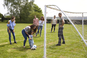 Mother with kid and adult friends playing on football pitch
