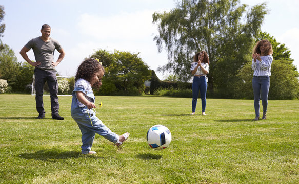 Mum and friends watch her daughter kicking a ball outdoors