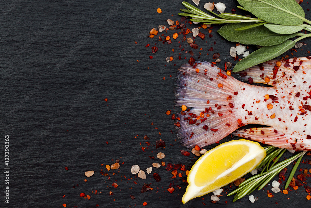 Wall mural Tail of fresh raw red tilapia fish on black slate stone board with spices, herbs, lemon and salt. Culinary seafood background. Top view, copy space