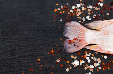 Tail of fresh raw red tilapia fish on black slate stone board with spices and pink himalayan salt....