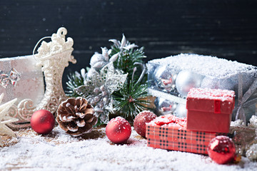 Holidays background. Toys and presents on a dark wooden background with a lot of snow. Pine cones, presents, Christmas balls and other toys on a snow background.