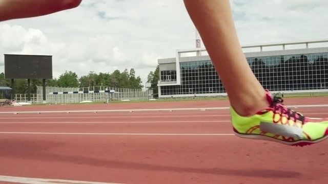 Tracking of female legs running along stadium track in summer