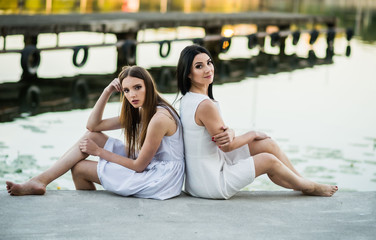 mother and daughter in white dresses sitting on a pier summer the evening