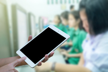 Hands woman are holding touch screen smart phone,tablet on blurred Defocused student study computer classroom background.