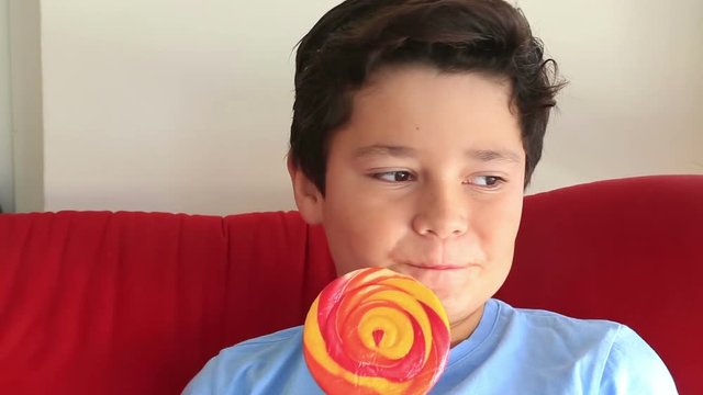 A boy in a blue shirt eating lollipop. Happy kid with a big candy