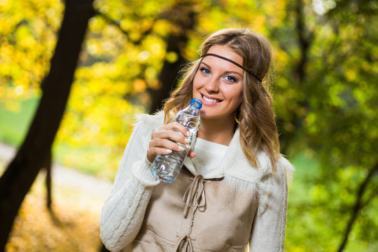 Beautiful boho girl enjoys drinking water in the park.