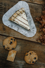 Chocolate cookies in a white plate on wooden background. Near cones and cinnamon stick, roughly. View from above. The theme of the new year holiday