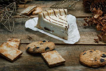 Beautiful homemade cake cheesecake on a white paper on the wooden background. Next chocolate chip cookies, Christmas gifts, Christmas tree, cones and toys. Conceived to celebrate the new year.