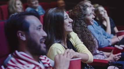Closeup of young couple sharing popcorn while watching comedy in movie theater - Powered by Adobe