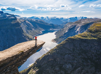 Young woman relaxon Trolltunga. Happy girl enjoy beautiful lake and good weather in Norway. - obrazy, fototapety, plakaty