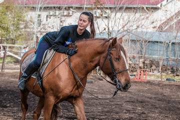 Young beautiful brunette girl rides a horse on a warm and sunny autumn day. Portrait of a pretty young woman on the horse, wearing tall boots and gloves.