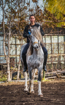 Young beautiful brunette girl rides a horse on a warm and sunny autumn day. Portrait of a pretty young woman on the horse, wearing tall boots and gloves.