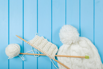 Knitted white scarf and hat on blue wooden background.