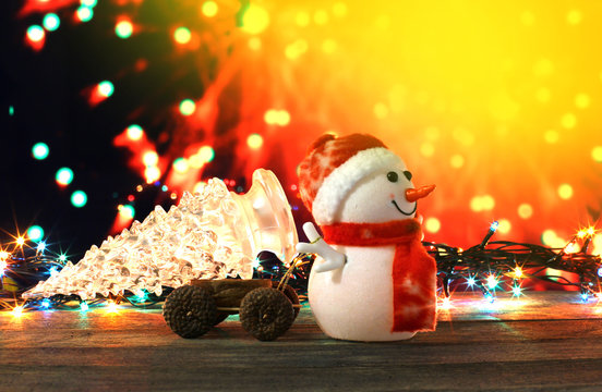 Dark evening Christmas and New Year`s card or poster with Snowman drags a truck glass tree on colorful bokeh background. Yellow copyspace for text, logo, sale price and item description on top corner.