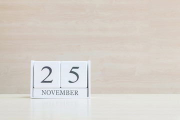 Closeup surface white wooden calendar with black 25 november word on blurred brown wood desk and wood wall textured background with copy space , selective focus at the calendar