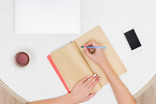 Female designer hands holding cup of hot beverage and working with laptop and notebook. Employee woman drinking morning tea of coffee. Coffeebreak during working day,  advertising business concept