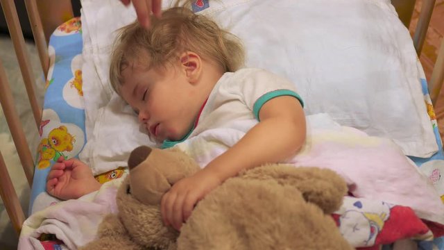 the sweet baby sleeps in a cot with a teddy bear.