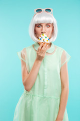 Cute blonde young woman standing and eating cupcake