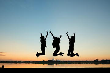 silhouette of young girl friends jumping with joy at sunrise or