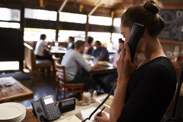Deurstickers Young woman taking a reservation by phone at a restaurant © Monkey Business