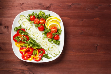 Salad with tomatoes, cucumbers, sweet peppers and onions on a square plate on a wooden table