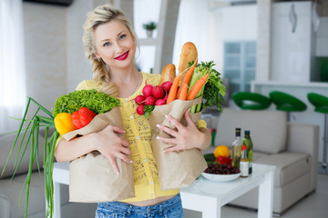 Housewife young beautiful woman the blonde with blue eyes,dressed in a yellow blouse,bright red lipstick,a beautiful manicure,light makeup,holding a paper bag with fresh vegetables and French baguette