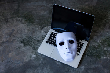 Anonymous mask to hide identity on computer laptop - internet criminal and cyber security threat concept