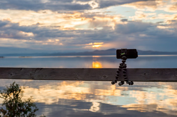 Obraz premium Smartphone attached on flexible tripod facing the sea at sunset