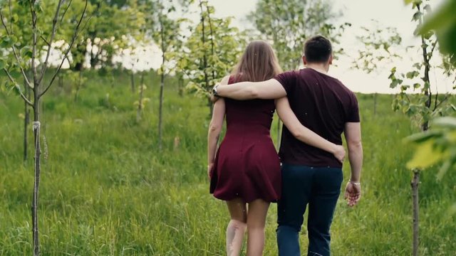 Backview of a loving couple walking in a garden. Hugging lovers enjoy nature Slow mo, steadicam shot