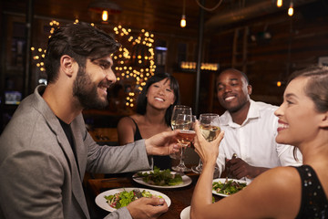 Four friends making a toast over dinner at a restaurant