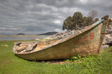 Old fiberglass boat pulled up into the grass by a lake in western Turkey