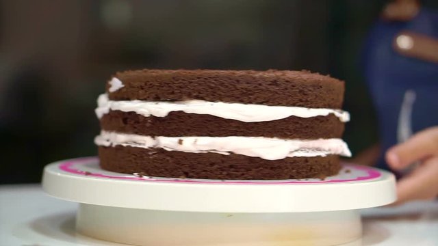 Patisserie chef baking decorating chocolate sponge cake. Putting white cream in the middle layers