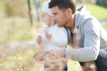 Daddy with baby girl picking flowers in countryside, autumn day