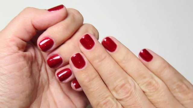 Young woman looks at her fresh glossy professional manicure. Close up of hands and fingers with beautiful red polish on short natural nails. Point of view shot. Real time full hd video footage.