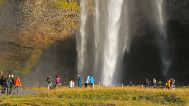 tourists are on foothill of waterfall Seljalandsfoss in Iceland in sunny autumn day