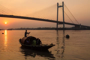 Foto op Canvas Wooden boat on river Hooghly at sunset with Vidyasagar bridge at the backdrop (silhouette), These country boats are used for pleasure boat rides on the river. © Roop Dey
