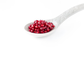 Closeup of pomegranate seeds on a large grey ceramic spoon isolated on white background.