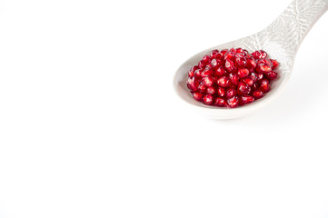 Pomegranate seeds on a large grey ceramic spoon isolated on white background with lots of copy space.