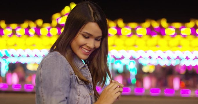 Smiling young woman at a colorful fairground standing in front of a bokeh of bright lights turning to smile at the camera