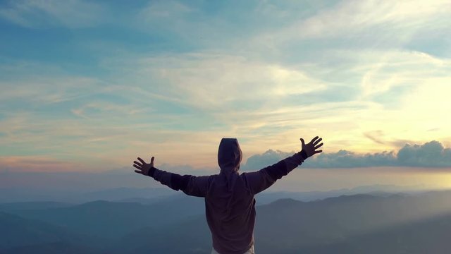 hiker on top of a mountain arms raised to the sky