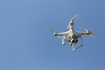 Quadcopter drone flying, blue sky background. No logos or trademarks.