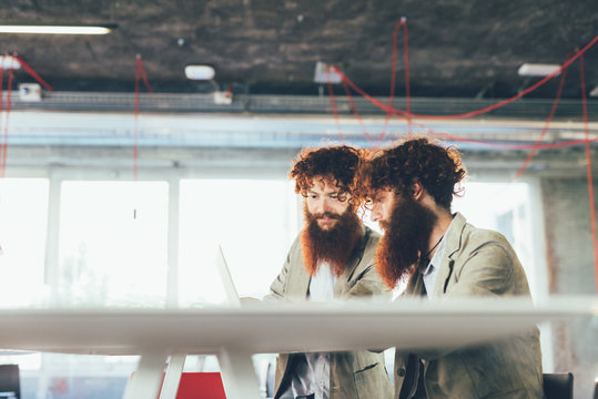 Male hipster twins working on laptop at office desk